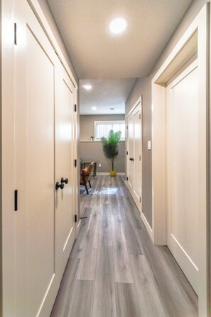 A hallway with wooden flooring, white doors, and a potted plant. - Modern Comfort in Westgate (Grande Prairie)