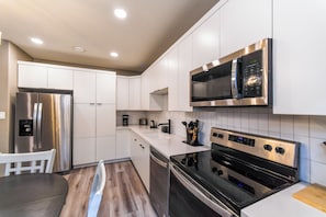 A modern kitchen with stainless steel appliances, white cabinetry, and a wooden dining table. - Modern Comfort in Westgate (Grande Prairie)