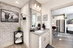 Un baño moderno con encimera de granito, un espejo grande y una pared de ladrillo.