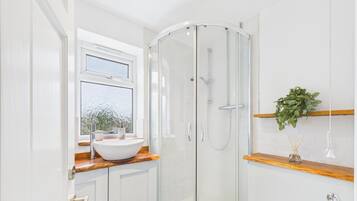 Une salle de bain moderne avec une douche à l’italienne en verre, un lavabo blanc doté d’un plan de toilette en bois et une fenêtre en verre dépoli.