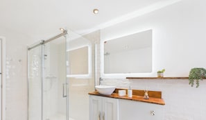 Ein modernes Badezimmer mit Duschkabine aus Glas, einem weißen Waschbecken und einem Spiegel über der Ablagefläche.
