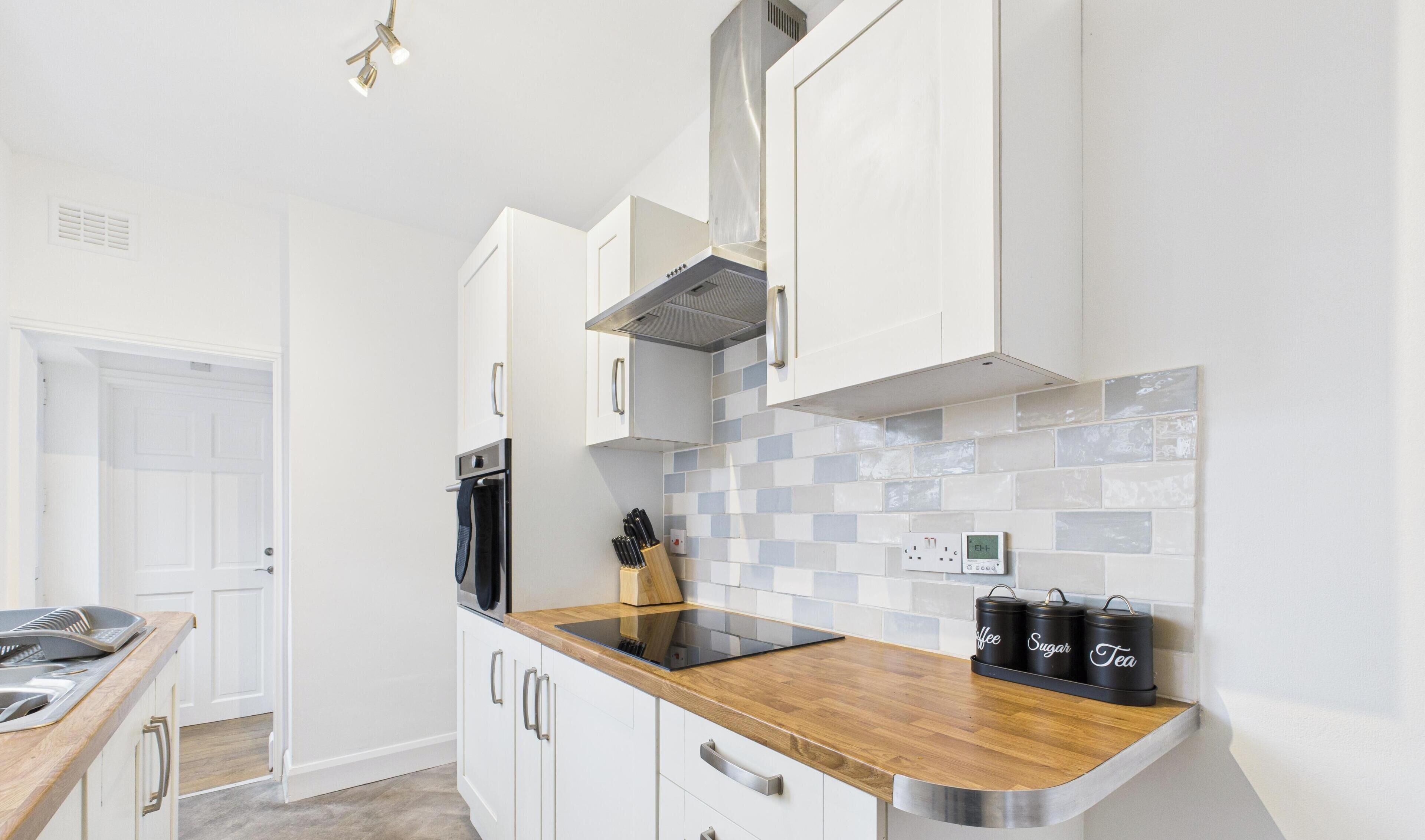 Una cocina moderna con armarios blancos, encimera de madera, horno empotrado y salpicadero de azulejos.