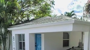 Un petit bâtiment blanc avec une porte bleue, un garage et une voiture garée.