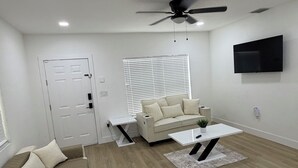 Un salon moderne avec un canapé, une table basse, un ventilateur de plafond et un téléviseur fixé au mur.