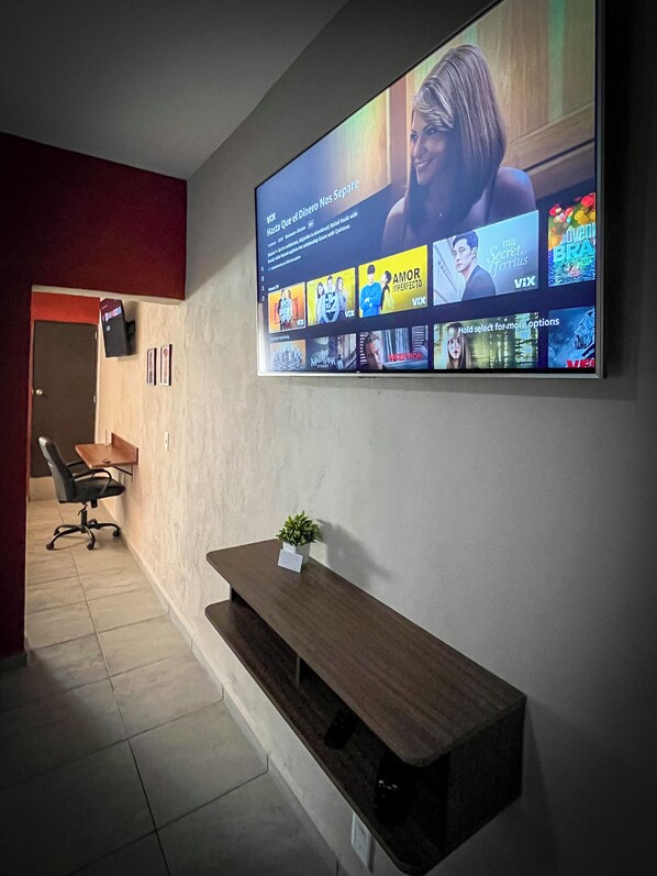 Una sala de conferències amb una pantalla gran que mostra una interfície de videoconferència, una banca de fusta i una petita planta.