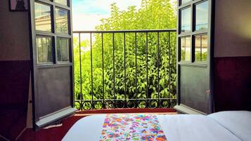 Una habitación con una cama, un ventanal con vistas abiertas a un balcón y una colcha de colores.