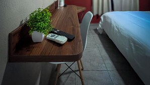 Une chambre d’hôtel avec un lit, un bureau agrémenté d’une plante, une télécommande et un téléviseur fixé au mur.