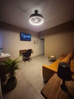 A modern living room with a flat-screen TV, a wooden coffee table, a sofa, a desk, and a potted plant.