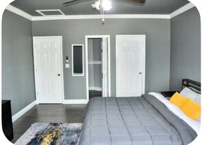 A bedroom with a bed, two doors, a ceiling fan, and a nightstand.