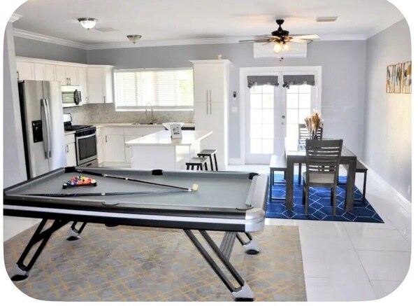 A pool table in a room with a kitchen, dining area, and a ceiling fan.