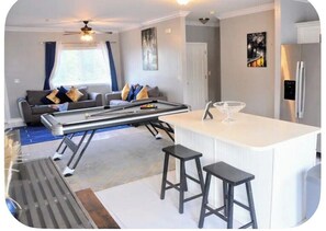 A modern living room with a sofa, a coffee table, and a kitchen area with a refrigerator and bar stools.