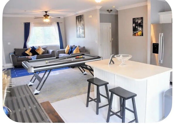 Una sala de estar moderna con un sofá, una mesa de centro y una zona de cocina con un refrigerador y taburetes de bar.