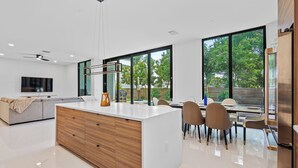 A modern kitchen with a large island, dining area with chairs, and a TV on the wall. - Stylish Pool Home 4BR Near Siesta Key "Palm Noir" (Sarasota)