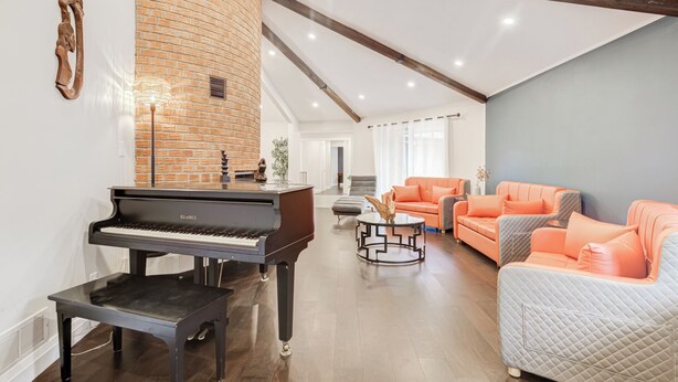 Un vaste espace de vie agrémenté d’un magnifique piano à queue, d’un mur en briques apparentes et d’un canapé moderne de couleur orange.