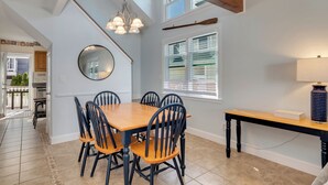 Un coin repas avec une table et des chaises en bois, un lustre, un miroir et une fenêtre avec des stores.