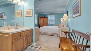 Une chambre à coucher avec un lit en bois, une table de chevet, une lampe, une commode et une fenêtre avec des stores.
