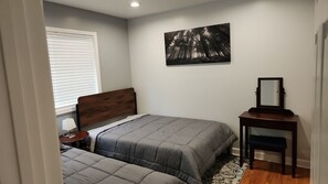 A bedroom with two beds, a nightstand, a desk with a mirror, and a painting on the wall. - Chicago Lakefront Vacation Rental · Fire Pit Patio · Loyola Beach (Chicago)