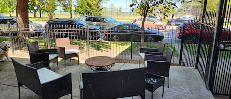 Un espace extérieur aménagé en patio, avec des meubles en osier et une table ronde, le tout entouré d’une clôture en métal.