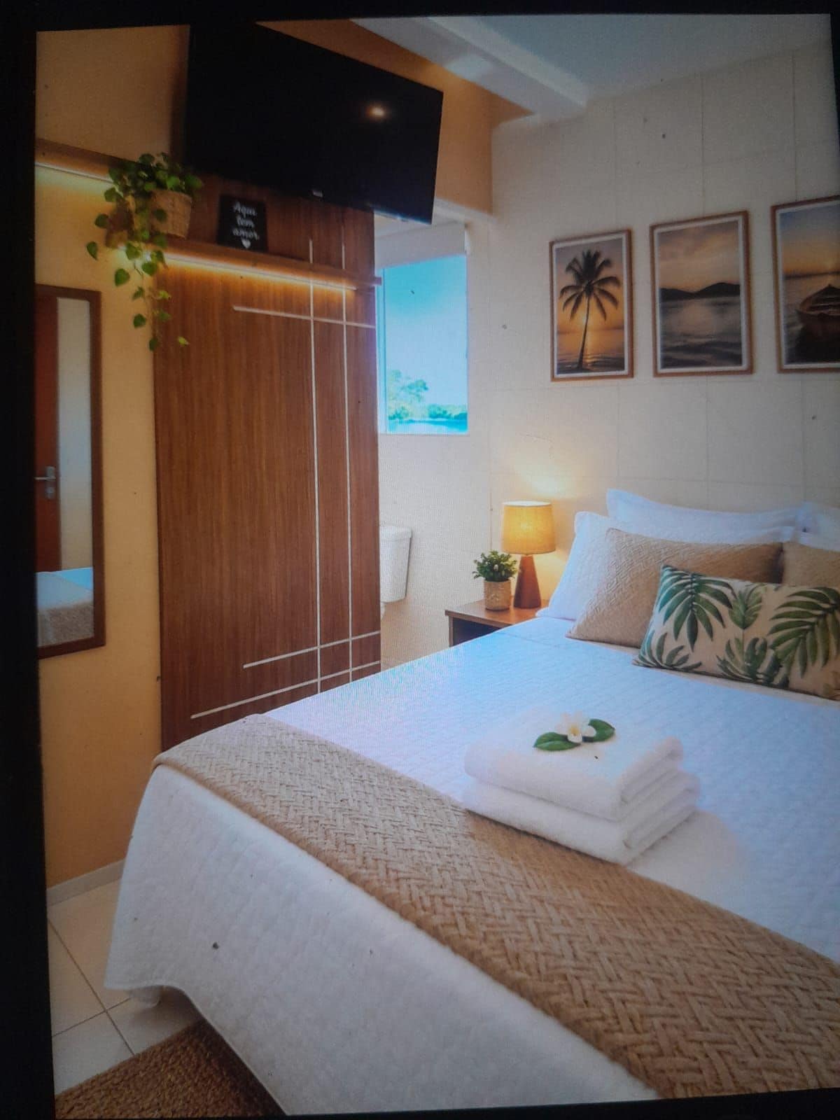 Ein Hotelzimmer mit Bett, Wandfernseher, Fenster mit Ausblick und einem kleinen Tisch mit Lampe.