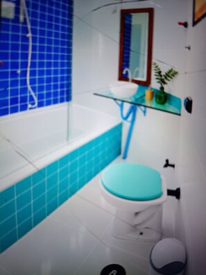 Een badkamer met een witte badkuip, een blauw toilet en een glazen wastafel.