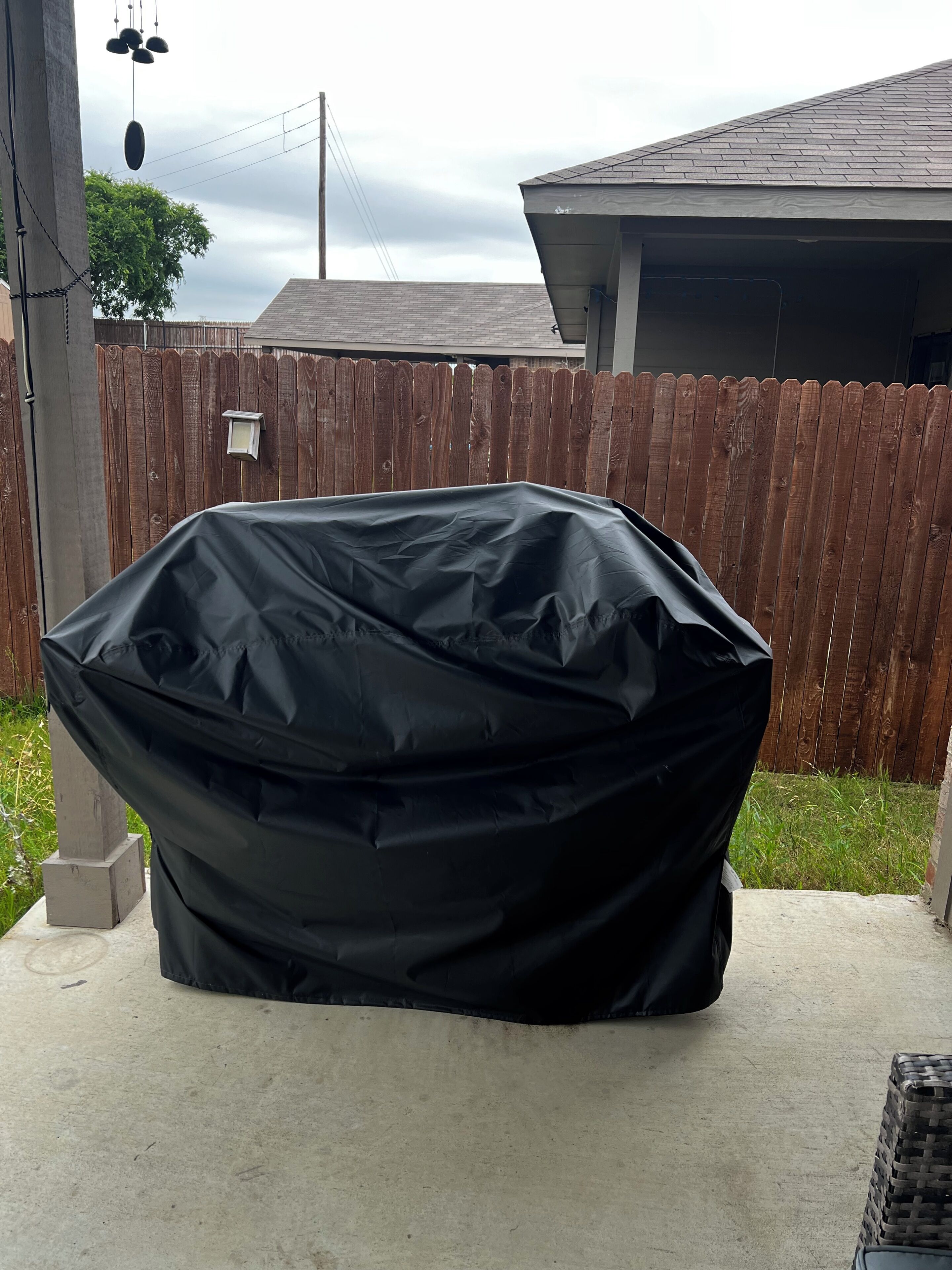 A covered grill in a backyard with a wooden fence and a house in the background.