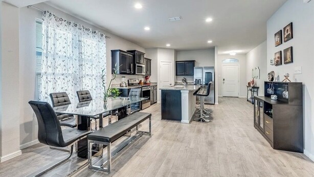 A modern kitchen with dark cabinets, a central island, and a dining area with a glass table and chairs.