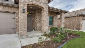 A residential building with a brick facade, a garage door, a front entrance with a door, and a landscaped garden area.