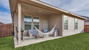 A house with a covered porch, two windows, a hammock, and a small outdoor seating area.