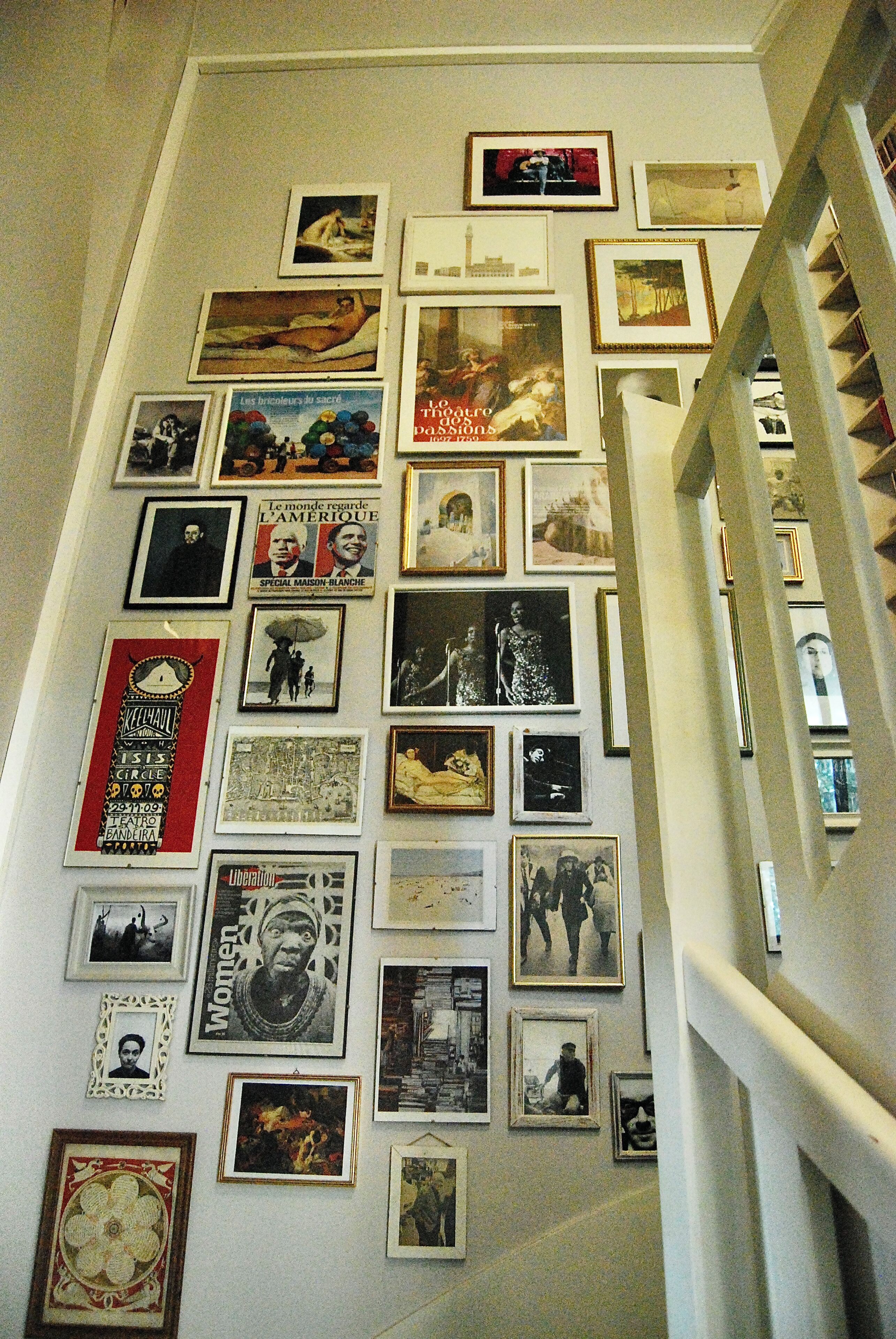 A wall with various framed pictures and posters, a staircase to the right, and a white wall.