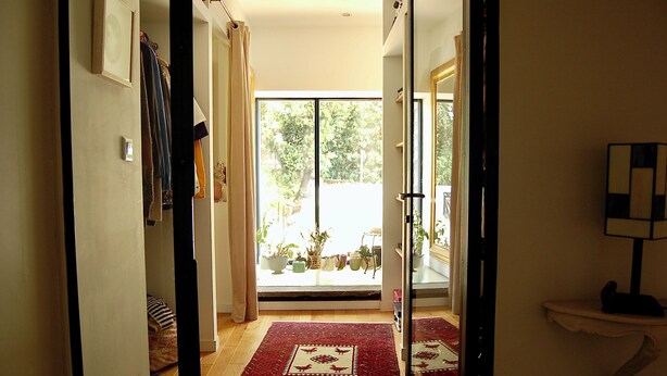 Un couloir mène à une pièce dotée d’une grande fenêtre, d’un tapis rouge et d’une porte avec un panneau de verre.