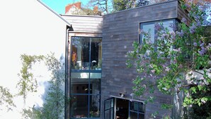 Un bâtiment moderne doté de grandes fenêtres, d’une façade en bois et d’un espace jardin agrémenté de plantes à fleurs.