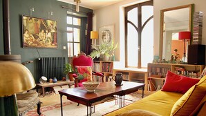 Une pièce comprenant un canapé, une table avec un saladier, une bibliothèque, un radiateur et un tableau accroché au mur.