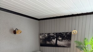A modern living room with a dark grey sofa, a white coffee table, a painting of trees, a potted plant, and a small table with a lamp. - Cosy apartment in a quiet neighborhood, close to beautiful nature. (Kópavogur)