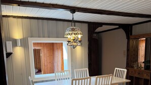 A dining area with a white table and chairs, a hanging light fixture, and a wooden ceiling. - Cosy apartment in a quiet neighborhood, close to beautiful nature. (Kópavogur)
