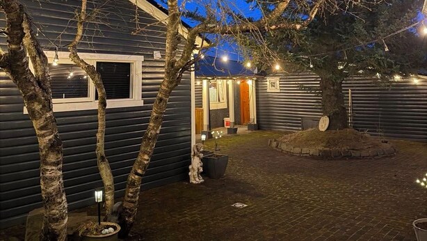 A cabin with a porch, a small garden with potted plants, and a tree in the foreground. - Cosy apartment in a quiet neighborhood, close to beautiful nature. (Kópavogur)