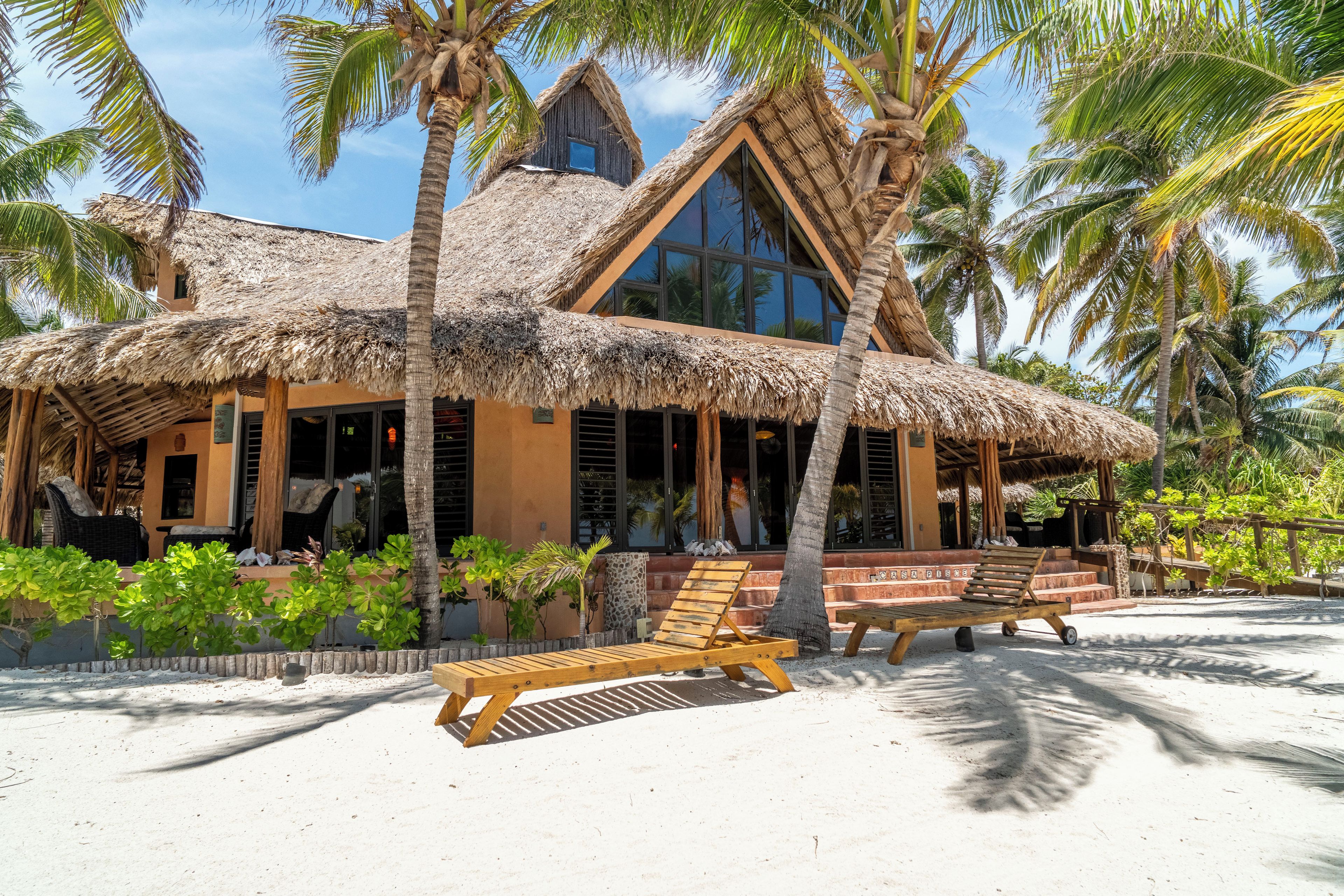 A beachfront building with a thatched roof, wooden deck, and palm trees.