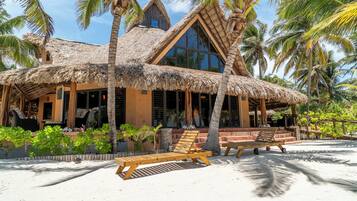 A beachfront building with a thatched roof, wooden deck, and palm trees.