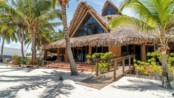 A beach house with a thatched roof, wooden deck, and palm trees.