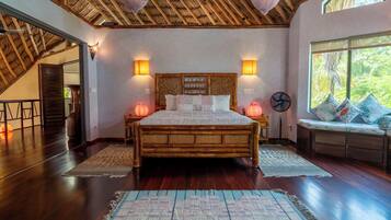A spacious bedroom with a large bed, wooden ceiling, and a view of greenery through a window.