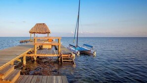 A wooden pier extending into calm waters with a thatched-roof structure and a sailboat docked nearby. - Casa Pisces (San Pedro)