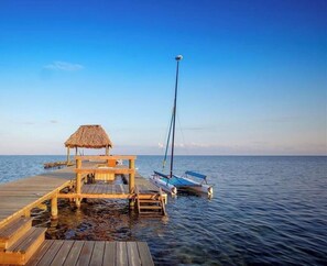 A wooden pier extending into calm waters with a thatched-roof structure and a sailboat docked nearby. - Casa Pisces (San Pedro)