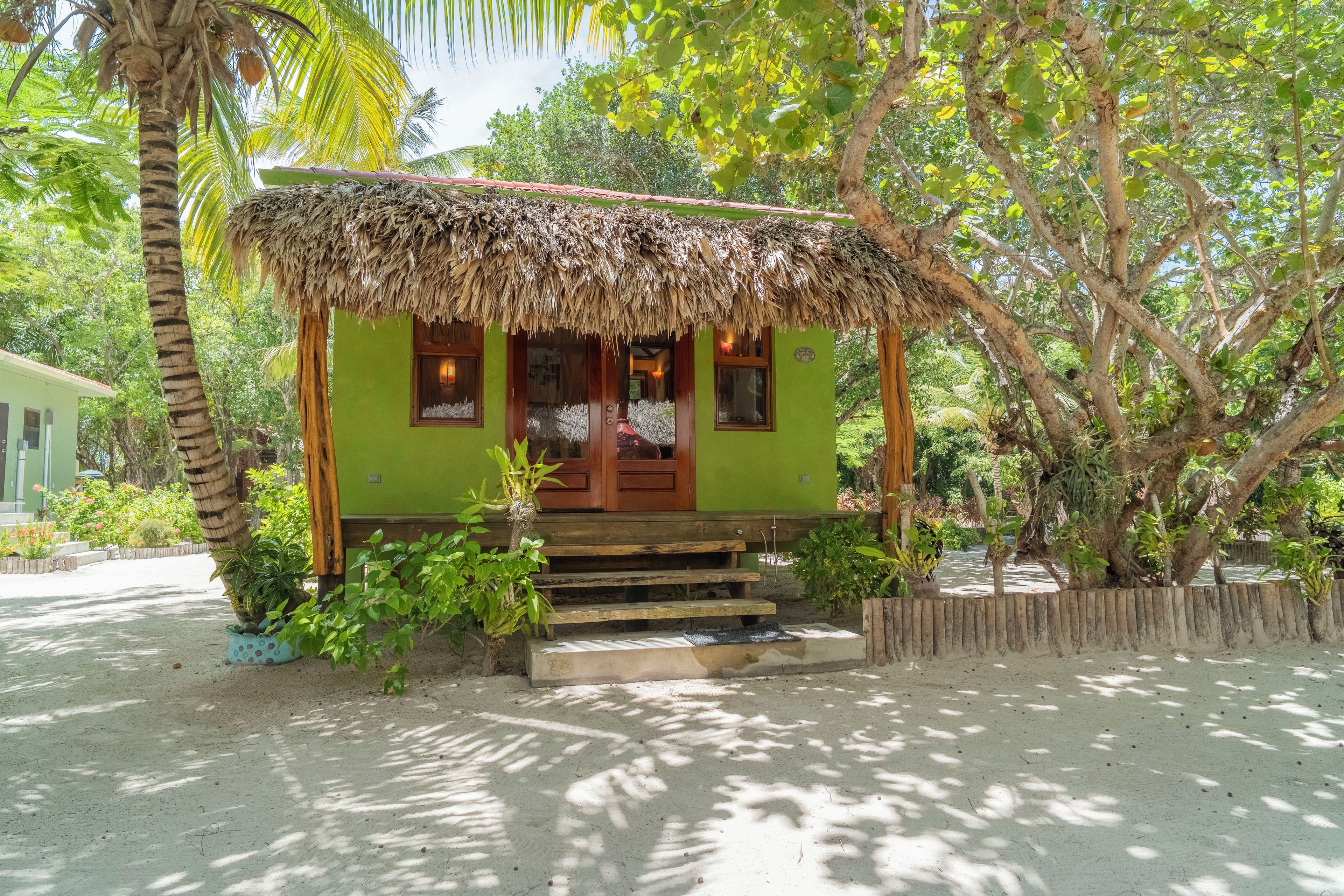 A small, single-story structure with a thatched roof, surrounded by lush greenery and trees.