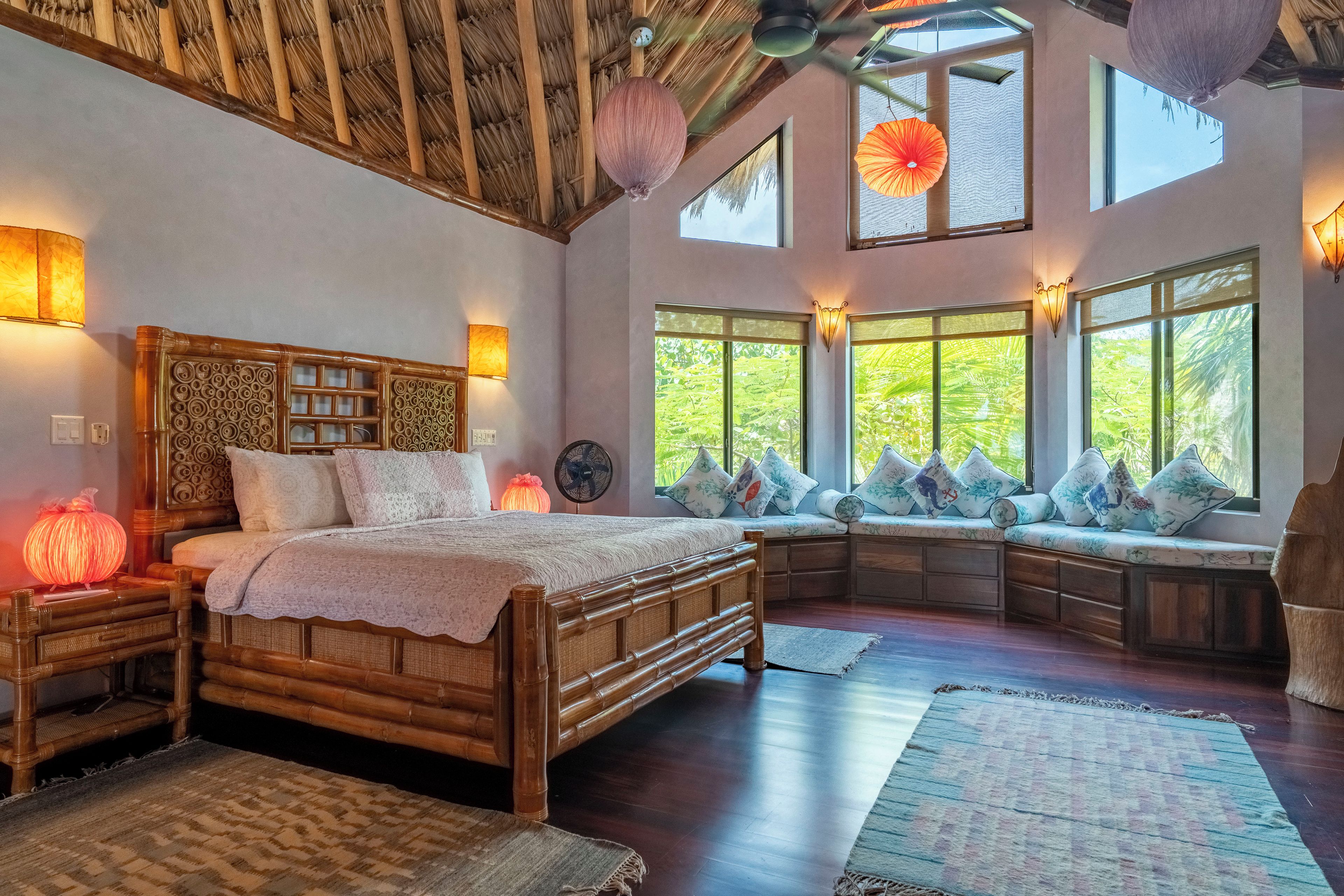 A room with a large bed, a bench with cushions, and a fan.