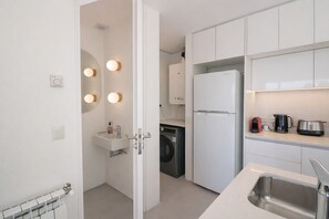 A modern kitchen with white cabinets, a built-in washing machine, a refrigerator, and a countertop with a kettle and a toaster. - Signature Lake View Luxury Residences A01 (San Carlos de Bariloche)
