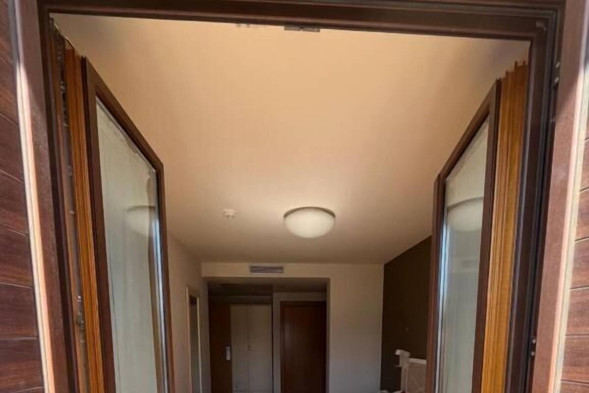 A hotel room with a bed, a nightstand, a mirror, and a door leading to another room.