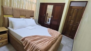 A bedroom with a bed, wooden nightstand, wardrobe, and a mirror. - Peaceful Central Stay at Pristine Homes (Kilimanjaro Region)