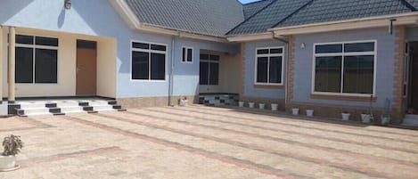A two-story building with a flat roof, large windows, and a paved courtyard.