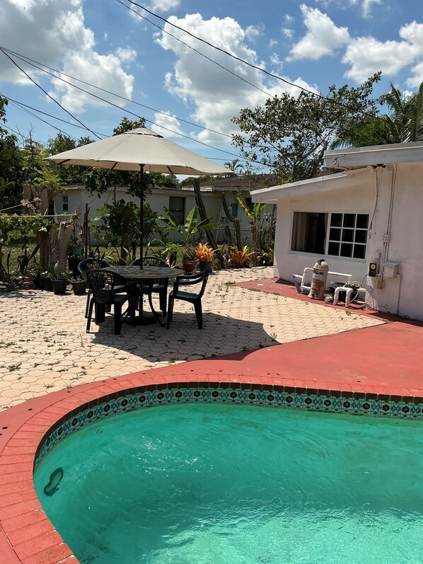 A swimming pool with a tiled edge, a patio area with a table and chairs, and a covered outdoor seating area. - Cozy Miramar 1 Bedroom with POOL for vacation, travel nurse short, longterm rent (Miramar)