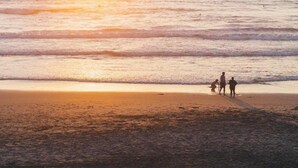A beach scene with a sunset, calm sea, and a few people walking along the shore. - Fantastic Holiday Home Near hot tub (Sint Maartensvlotbrug)