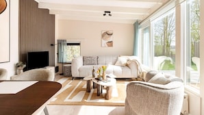 A modern living room with a sofa, coffee table, and a large window. - Fantastic Holiday Home Near hot tub (Sint Maartensvlotbrug)